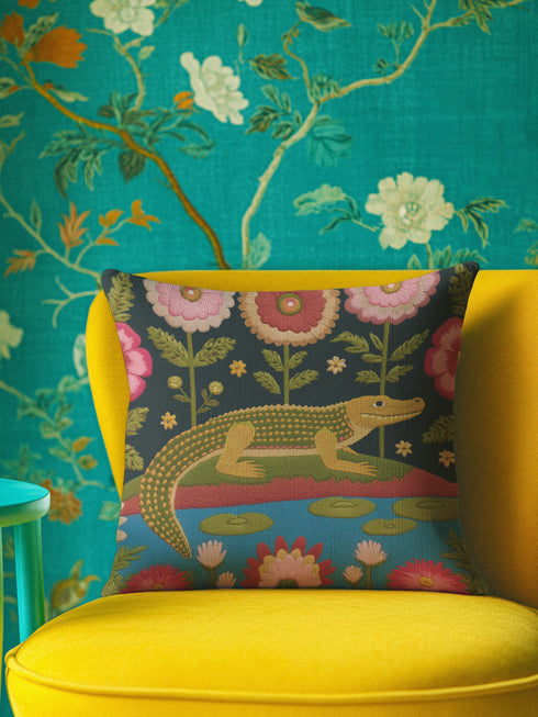 A vibrant square throw pillow cover featuring a green alligator illustration on a dark charcoal background. The design mimics the texture of vintage needlepoint embroidery on faux linen fabric. The alligator is accented with lime green scales and hot pink floral and lip motifs, creating a maximalist junglecore aesthetic. The pillow is shown on a furniture piece, highlighting the vivid cherry red and neon accents typical of dopamine decor and swampcore styles.