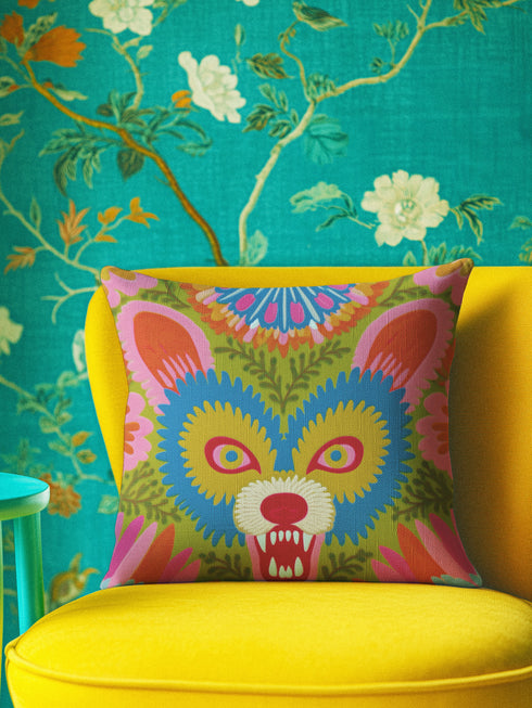 A square throw pillow cover featuring a vibrant, symmetrical illustration of an angry opossum face. The design mimics the texture of folk art embroidery but is a smooth flat print on faux linen fabric. The possum features teal blue fur, bright yellow eyes with pink pupils, and a red nose, bearing sharp white teeth in a hiss or scream. The background is a mossy green with pink and orange floral accents surrounding the animal. The style is maximalist, eclectic, colorful, and feral core aesthetic.