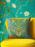 A square decorative throw pillow cover featuring a detailed illustration of a green tiger face in an Art Nouveau style. The tiger has piercing blue eyes and a bright orange nose, surrounded by intricate swirling botanical leaves in shades of teal and sage. The design mimics the look of embroidery or needlepoint but is a flat print on textured faux linen fabric. The background is a deep blue-green. The image is symmetrical and bold, fitting maximalist or junglecore aesthetics
