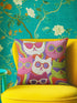 Square throw pillow cover packed with a dense repeating pattern of cat faces in hot pink, lime green, purple, and white, every cat wearing oversized retro sunglasses. Wavy psychedelic bands of orange, yellow, and green weave through the background. The flat 2D print mimics heavy textured crewel needlepoint on a smooth, linen-feel fabric. Reversible same design front and back with a hidden zipper. Funky maximalist cat decor and quirky apartment warming gift, available in 18 by 18 inch and 22 by 22 inch, cove