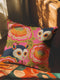 A square linen-feel throw pillow with a vibrant, maximalist print on a bright pink background. The pattern features two large, illustrated possums (or sugar gliders). The animals are nestled amongst large, 70s-style retro floral designs in shades of orange, marigold yellow, and turquoise, with avocado green leaves. The pillow has a textured, woven appearance, mimicking a high-end linen fabric. The double-sided print is colorful, eclectic, and groovy, with a distinct vintage 70s folk art feel.