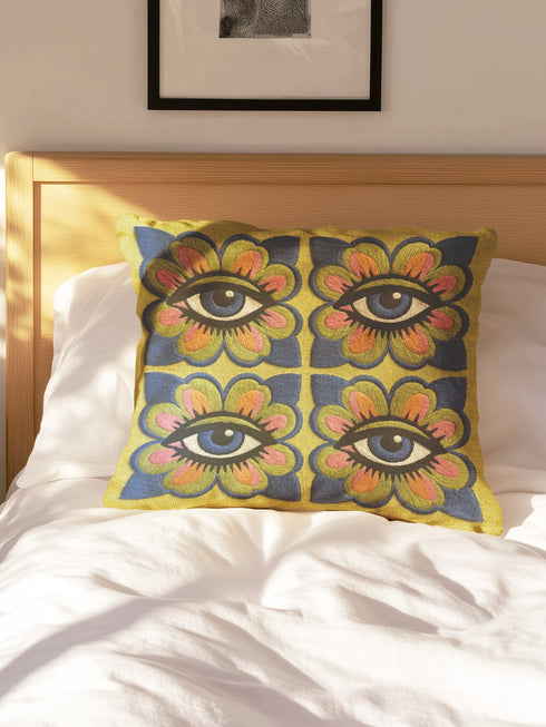 Square double-sided throw pillow cover featuring a vibrant faux embroidery design. Four stylized blue eyes sit inside retro pink, green, and orange floral shapes against a textured chartreuse yellow-green background. Made from premium faux linen polyester with a clean hidden zipper edge. This maximalist dopamine decor cushion cover is shown perfectly flat, highlighting the bold surrealist trompe-l'œil graphic print. Available in 18x18 or 22x22 inches.
