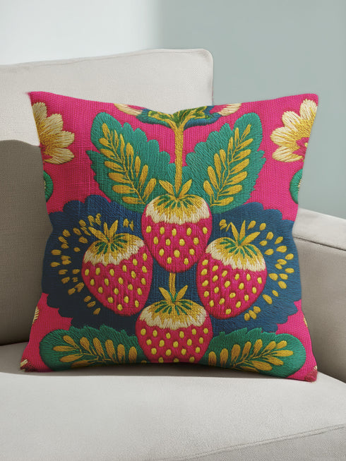 A square throw pillow with a vibrant, folk art-inspired design. The pillow's background is a bright, saturated fuchsia pink. The central design features four stylized strawberries arranged in a cluster, rendered in a way that mimics thick, textural embroidery. Each strawberry is red. The overall aesthetic is colorful, eclectic, and maximalist, with a distinct retro or 70s feel. The pillow cover has a visible linen-like texture.