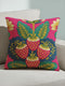 A square throw pillow with a vibrant, folk art-inspired design. The pillow's background is a bright, saturated fuchsia pink. The central design features four stylized strawberries arranged in a cluster, rendered in a way that mimics thick, textural embroidery. Each strawberry is red. The overall aesthetic is colorful, eclectic, and maximalist, with a distinct retro or 70s feel. The pillow cover has a visible linen-like texture.