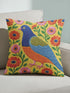 Square faux embroidery throw pillow cover with a large stylized folk art bird facing left. The bird has a cobalt blue head, orange belly, light blue tail, and pink legs, set on a bright mustard yellow background scattered with pink and red daisy flowers on trailing green vines. The smooth, linen-feel polyester uses a printed trompe loeil effect to mimic raised thread needlework. Bold maximalist folk art bird pillowcase and cottagecore cushion cover for eclectic, colorful, dopamine decor homes.