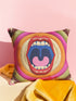 A square decorative pillowcase featuring a bold, centralized trompe-l'œil design printed to look like raised satin-stitch embroidery. The focal point is a large, open mouth with red lips, yellow teeth, and a pink tongue against a dark blue background. The mouth is surrounded by concentric radial rings in bright pink, orange, yellow, and olive green. The four corners are a dark burgundy brown, each accented with a yellow four-pointed starburst. The fabric has a woven linen-like texture.