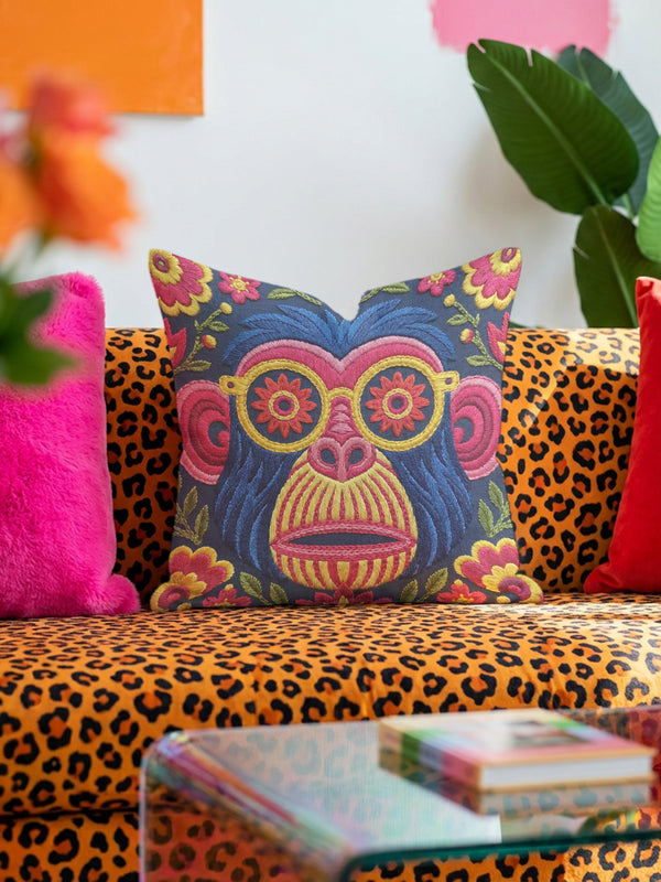 quare throw pillow cover with a faux embroidery 2D print of a stylized monkey face in large round yellow sunglasses with red flower lenses. The ape has electric blue fur with a hot pink brow and nose, on a navy background scattered with hot pink, yellow, and red flowers and green leaves. The print mimics raised stitching while staying flat and smooth, and shows on both sides. Cover only, available in 18 by 18 inch and 22 by 22 inch sizes.