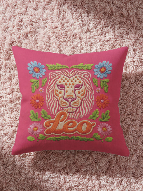 Maximalist throw pillow for the Leo zodiac sign featuring a centralized lion head medallion with an ornate mane mimicking embroidered textures. The background is a vibrant hot pink, accented by ochre, rust, and lime green floral motifs and blue flowers in each corner. The pillow is square with a hidden zipper and a polyester insert. This high-contrast design is a perfect fit for dopamine decor, whimsigoth apartments, or any eclectic home looking for a bold astrology-inspired statement piece.