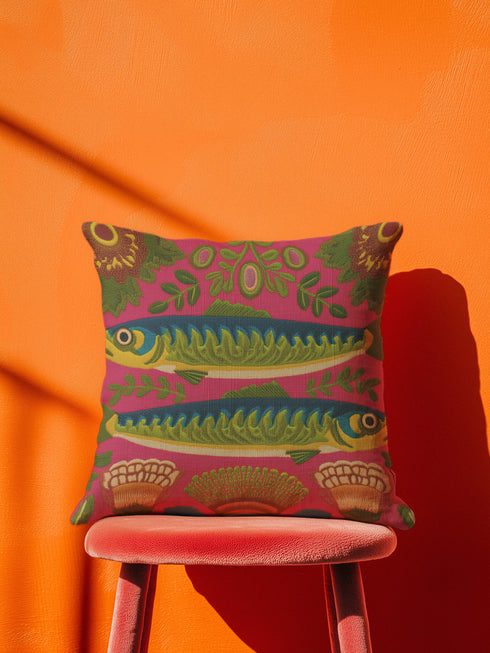 A square throw pillow cover featuring a symmetrical maximalist design on a hot pink background. Two stylized green and blue sardines swim in opposite directions in the center, featuring detailed scales and yellow eyes. The fish are surrounded by a folk art style pattern of green leafy vines and stylized orange and yellow flowers at the corners. The fabric has a faux linen texture with a flat printed design that mimics the look of vintage embroidery. Vibrant colors include pink, green, blue.