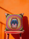 A square decorative pillowcase featuring a bold, centralized trompe-l'œil design printed to look like raised satin-stitch embroidery. The focal point is a large, open mouth with red lips, yellow teeth, and a pink tongue against a dark blue background. The mouth is surrounded by concentric radial rings in bright pink, orange, yellow, and olive green. The four corners are a dark burgundy brown, each accented with a yellow four-pointed starburst. The fabric has a woven linen-like texture.