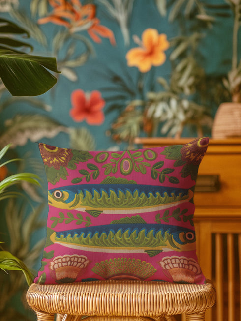 A square throw pillow cover featuring a symmetrical maximalist design on a hot pink background. Two stylized green and blue sardines swim in opposite directions in the center, featuring detailed scales and yellow eyes. The fish are surrounded by a folk art style pattern of green leafy vines and stylized orange and yellow flowers at the corners. The fabric has a faux linen texture with a flat printed design that mimics the look of vintage embroidery. Vibrant colors include pink, green, blue.
