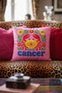 A square pink pillowcase features a vibrant, multi-colored design centered around a yellow and red crab representing the Cancer zodiac sign. The design is framed by symmetrical green leaves and yellow and red flowers. The word "cancer" is written in a bold, blue, rounded font at the bottom. The visual texture mimics intricate raised embroidery with visible stitch patterns, though the surface is a smooth 2D print on a linen-textured polyester fabric with a hidden zipper.