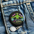 Round black pinback button featuring lime green female figure with outstretched arms and purple floral details, surrounded by pink flowers and blue blooms with multicolored "MY BODY MY RIGHTS" text. Folk art feminist pin with glossy finish and safety pin backing in 2" and 3" sizes.