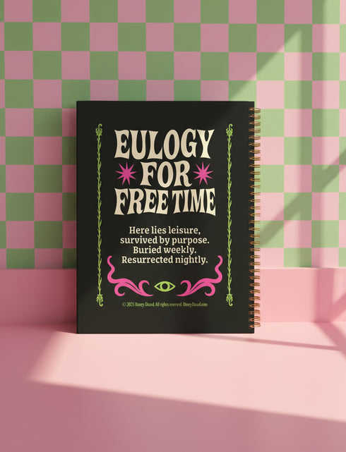 A black hardcover spiral planner. The cover features a vibrant, coffin-shaped frame in lime green and magenta pink, bordered by thorny vines. Inside the frame, the title "Obituary of Free Time" is written in a psychedelic 70s-style font. Below the title, a pink flower with a single green eyeball at its center blooms from a thorny stem. The planner is bound with a gold metal wire-o spiral on the left side. The design has a spooky cute, gothic floral aesthetic.