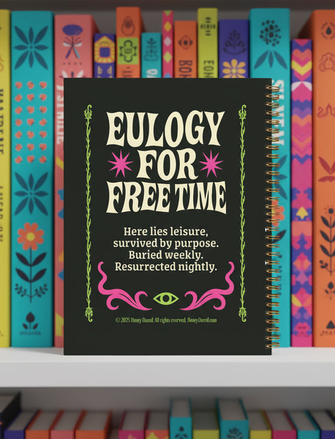 A black hardcover spiral planner. The cover features a vibrant, coffin-shaped frame in lime green and magenta pink, bordered by thorny vines. Inside the frame, the title "Obituary of Free Time" is written in a psychedelic 70s-style font. Below the title, a pink flower with a single green eyeball at its center blooms from a thorny stem. The planner is bound with a gold metal wire-o spiral on the left side. The design has a spooky cute, gothic floral aesthetic.