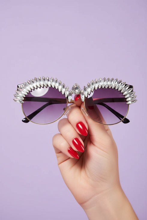 Sunglasses with decorative metal frame held by a hand against a purple background