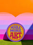 A round embroidered patch with the words "MAKE MORE ART" in a retro 70s psychedelic font. The word "ART" is magenta pink, "MAKE MORE" is purple, and they are set against a bright yellow circular background. The entire design is encircled by a thin pink line and a thick purple border. This 3-inch iron-on applique is a colorful, groovy accessory for DIY projects, perfect for personalizing jackets, backpacks, or denim vests. It serves as an inspirational artist gift with a vintage aesthetic.