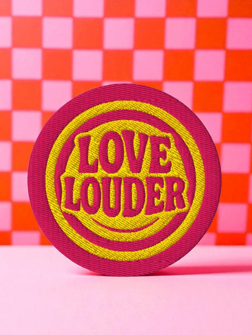 A round, 3-inch embroidered Love Louder patch designed with a vibrant, retro 70s aesthetic. The design features groovy, puffy-style text in a bright, sunny yellow thread, set against a bold magenta pink twill fabric background. The words 'LOVE LOUDER' are stacked to fill the center, encircled by concentric yellow rings that create a hypnotic, radiating effect. The entire circular patch is finished with a clean, durable merrowed border.