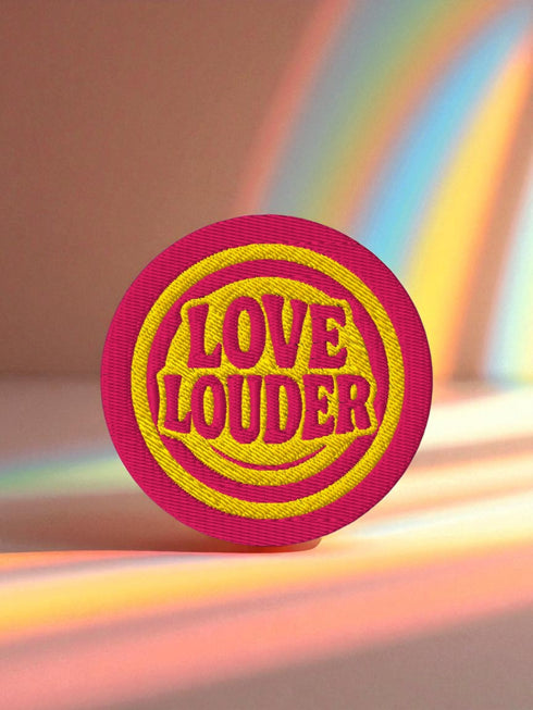 A round, 3-inch embroidered Love Louder patch designed with a vibrant, retro 70s aesthetic. The design features groovy, puffy-style text in a bright, sunny yellow thread, set against a bold magenta pink twill fabric background. The words 'LOVE LOUDER' are stacked to fill the center, encircled by concentric yellow rings that create a hypnotic, radiating effect. The entire circular patch is finished with a clean, durable merrowed border.