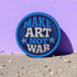 Round embroidered iron-on patch featuring "MAKE ART NOT WAR" text with blue floral design. Navy blue background with light blue border, white cream lettering, and small yellow-centered blue flowers. 3-inch circular twill fabric patch perfect for jackets, backpacks, denim, and clothing customization. Anti-war peace activist feminist punk alternative accessory for creative counterculture gift giving.