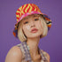 A reversible bucket hat with two distinct sides. Side one features a red and yellow zebra pattern with large pink and orange daisies. Side two has a deep purple background with white stars, rainbow scalloped bands in blue, green, and orange, and retro black and white flowers. The fabric has a visible textured linen weave. The hat is shown in a structured, professional studio shot against a white background, highlighting its 100% polyester durability.