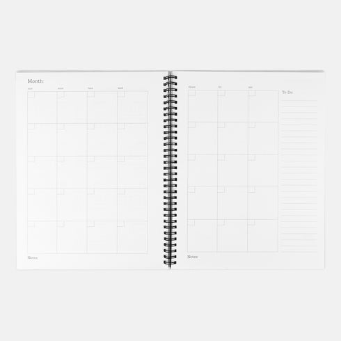 A sage green hardcover spiral planner for 2026 with the title "The 2026 Planner of Controlled Chaos" in a funky, retro 70s-style font. The cover features a groovy illustration of orange and pink flowers in a vase, with one flower depicted as an eyeball. The text reads "Bloom where you're planted. Or just wilt artfully." and "Notes from the Void." The planner has a gold metal wire-o binding. The back cover shows a decorative floral frame with a "Property Of" section