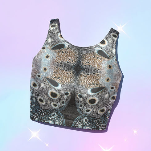 A women's sleeveless racerback crop top with a body-hugging fit. The top features a detailed, kaleidoscopic all-over print inspired by deer pelt. The symmetrical, Rorschach-like design includes abstract spots and textures in shades of brown, blue, black, and grey, creating an intricate pattern that resembles a deer pelt.