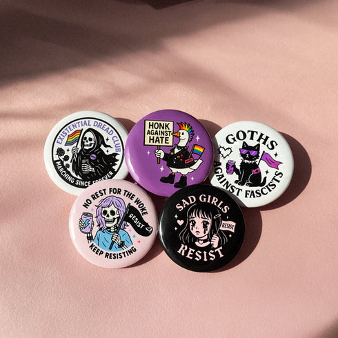 Set of 5 anti-fascist resistance pinback buttons featuring "Sad Girls Resist," "Goths Against Fascists," "Existential Dread Club," "Honk Against Hate," and "No Rest for the Woke" designs. Each pin measures 2.25" diameter. Made with durable tinplate and scratch-resistant mylar coating. Perfect protest accessories for activists, anti-fascist supporters, and LGBTQ+ allies. Express your resistance with these statement pins.