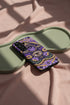 A matte finish phone case featuring a 2D optical illusion of a textured, purple crochet Ouija board planchette. The design includes intricate gold faux-embroidered borders, the words YES and NO, a central all-seeing eye, and a botanical leaf motif in the center circle. Lilac purple flowers and green leaves decorate the bottom half. The case has black rubber lining around the edges and camera cutouts. It looks like a thick, handmade yarn textile but is completely flat and smooth.
