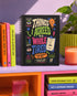 A black hardcover undated planner with black wire spiral binding. The front cover displays a bold, colorful typographic layout reading: "THINGS I AGREED TO WHILE TIRED". Surrounding text includes "LATE-NIGHT DECISIONS VOLUME 1", "ZERO MEMORY OF THIS.", and "A PRACTICAL GUIDE TO POOR TIMING." The back cover reads "INSIDE THIS DEEPLY SUSPICIOUS VOLUME:" above five colored banner rows detailing space for plans, notes for spirals, room for lists, daily proof time is fake, and a paper trail of mistakes.