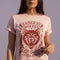 Vintage style graphic t-shirt with a large snarling wolf face printed in dark charcoal ink. A curved banner above reads RAISED BY WOLVES and a banner below reads RADICALIZED BY LEGISLATION, framed by stylized flames and scattered stars. Classic crewneck short sleeve cotton tee with a relaxed fit and seamless sides, available in soft pink, pale green, and ivory. Feminist protest apparel and activist statement tee for reproductive rights, marches, and everyday quiet rage.