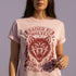 Vintage style graphic t-shirt with a large snarling wolf face printed in dark charcoal ink. A curved banner above reads RAISED BY WOLVES and a banner below reads RADICALIZED BY LEGISLATION, framed by stylized flames and scattered stars. Classic crewneck short sleeve cotton tee with a relaxed fit and seamless sides, available in soft pink, pale green, and ivory. Feminist protest apparel and activist statement tee for reproductive rights, marches, and everyday quiet rage.