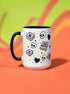 A white ceramic mug with a black interior and black C-shaped handle. The mug features a full wrap-around design in a pastel goth style. The repeating pattern includes cartoon illustrations of white skulls, black stitched hearts, and pastel purple books with an 'X' on the cover. One book is open and displays the words 'READ DANGEROUSLY'. The graphics are scattered with small pastel purple and pale yellow-green stars, creating a spooky and cute aesthetic.