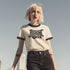 Heather gray ringer t-shirt with black contrast trim on the collar and sleeve cuffs. The front features a bold black graphic of an open mouth with the phrase "EAT THE RICH" in capital letters, integrated into the teeth. Surrounding the design are hand-drawn lines and accents, giving it a raw, punk-inspired aesthetic. The t-shirt has a vintage-inspired fit, made from soft cotton fabric with a slightly relaxed silhouette. The high-contrast black and gray design enhances the statement-making impact of the grap