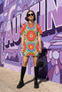 Short sleeve crew neck t-shirt dress on a cream background with an allover retro mod flower medallion print. Bold 60s daisies in red, yellow, and white sit at the center of concentric rainbow rings in lime green, hot pink, orange, and royal blue, with small magenta squares and tiny red checkerboard accents between the motifs. Above-the-knee straight fit silhouette in a 95 percent cotton, 5 percent elastane heavyweight stretch blend. Groovy retro flower power dress for dopamine dressing and easy summer outfi