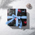 Christmas wrapping paper with a black background featuring colorful, stylized reindeer and Santa's sleigh designs. The reindeer and sleigh silhouettes are filled with skeletal patterns in shades of blue, pink, and red. Multicolored snowflakes in various sizes are scattered throughout. The paper has a whimsical, slightly gothic aesthetic that blends traditional holiday imagery with a unique, edgy twist.