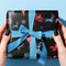 Christmas wrapping paper with a black background featuring colorful, stylized reindeer and Santa's sleigh designs. The reindeer and sleigh silhouettes are filled with skeletal patterns in shades of blue, pink, and red. Multicolored snowflakes in various sizes are scattered throughout. The paper has a whimsical, slightly gothic aesthetic that blends traditional holiday imagery with a unique, edgy twist.