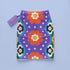 Form-fitting bodycon mini skirt with a mid-rise elastic waistband, falling to mid-thigh in smooth stretch fabric. It features a bold groovy mod floral print: oversized orange flowers with white inner petals and golden yellow centers, black flower accents, and white four-point sparkles, all set on a deep purple background. Rainbow borders in blue, green, orange, and yellow run down each side. The all-over design is a flat dye-sublimated print, available in a smooth knit or glitter knit finish.
