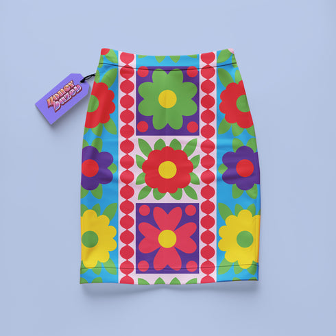 Form-fitting bodycon mini skirt with a mid-rise elastic waistband, falling to mid-thigh in smooth stretch fabric. It features a bold retro patchwork floral print: large mod daisies in red, purple, yellow, and green, set on a sky blue background with scattered green leaves. A central column frames single flowers on purple and pink tiles, edged by red and pink beaded borders. The all-over design is a flat dye-sublimated print, available in a smooth knit or glitter knit finish.