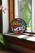 A round embroidered patch with a black background featuring the phrase “STAY WEIRD” in bold, multicolored lettering. "STAY" is stitched in a gradient of red, orange, and yellow, while "WEIRD" is in white. Surrounding the text are wavy, neon-like lines in blue, pink, yellow, and orange, creating a vibrant, psychedelic effect. The patch has a thick black border and is designed for iron-on or sew-on application, making it perfect for jackets, backpacks, denim, and accessories.