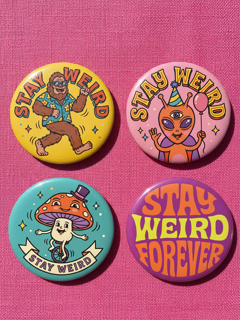 Set of 4 bright retro pinback buttons 2.25 inch. 1: Yellow button with cartoon Bigfoot in blue Hawaiian shirt and sunglasses striding under "Stay Weird" text. 2: Pink button with orange three-eyed alien in party hat holding a balloon. 3: Teal button with smiling mushroom in top hat riding a unicycle with "Stay Weird" banner. 4: Purple button with orange and yellow psychedelic 70s font reading "Stay Weird Forever." High gloss finish metal pins for backpacks, jackets, and weirdcore gifts.