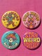 Set of 4 bright retro pinback buttons 2.25 inch. 1: Yellow button with cartoon Bigfoot in blue Hawaiian shirt and sunglasses striding under "Stay Weird" text. 2: Pink button with orange three-eyed alien in party hat holding a balloon. 3: Teal button with smiling mushroom in top hat riding a unicycle with "Stay Weird" banner. 4: Purple button with orange and yellow psychedelic 70s font reading "Stay Weird Forever." High gloss finish metal pins for backpacks, jackets, and weirdcore gifts.