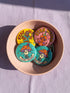 Set of 4 bright retro pinback buttons 2.25 inch. 1: Yellow button with cartoon Bigfoot in blue Hawaiian shirt and sunglasses striding under "Stay Weird" text. 2: Pink button with orange three-eyed alien in party hat holding a balloon. 3: Teal button with smiling mushroom in top hat riding a unicycle with "Stay Weird" banner. 4: Purple button with orange and yellow psychedelic 70s font reading "Stay Weird Forever." High gloss finish metal pins for backpacks, jackets, and weirdcore gifts.