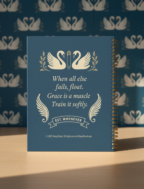 An 8.5 x 11 hardcover spiral planner with a durable satin-matte finish. The front cover is a deep navy blue, featuring elegant cream-colored text and vintage-style illustrations of two swans. A sturdy gold metal wire-o spiral binds the planner on the right side. This undated weekly and monthly goal organizer serves as a motivational journal for women, a self-care tracker, and a funny office supply. The celestial swan design gives it a unique, 70s retro aesthetic for organization.