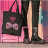 Canvas tote bag featuring pink skull cherries design. Two pink skulls connected by red stem and bow. Quirky gothic-inspired graphic on cream background. Stylish, edgy accessory for everyday use. Perfect for alternative fashion lovers.