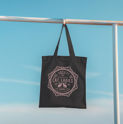 Election 2024 Canvas tote bag featuring a circular design with two cats and text "The Society of Childless Cat Ladies Against Couch Fuckers" in burgundy on a natural or black.