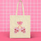 Canvas tote bag featuring pink skull cherries design. Two pink skulls connected by red stem and bow. Quirky gothic-inspired graphic on cream background. Stylish, edgy accessory for everyday use. Perfect for alternative fashion lovers.