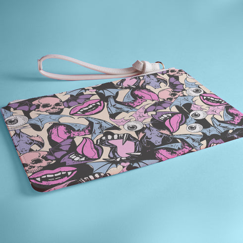 Rectangular wristlet clutch featuring a dark background with colorful bats, skulls, eyeballs, and vampire mouths. White strap and gold zipper visible.