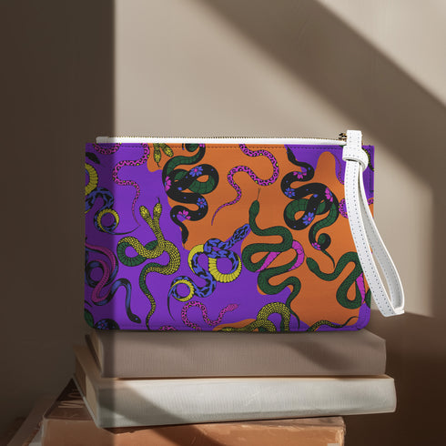 Rectangular wristlet clutch featuring vibrant purple and orange background with colorful snake prints. White strap and gold zipper visible.