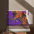 Rectangular wristlet clutch featuring vibrant purple and orange background with colorful snake prints. White strap and gold zipper visible.